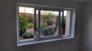 A window with a view of a courtyard with potted plants and a brick wall. - Pensión Las Matillas (Miranda de Ebro)