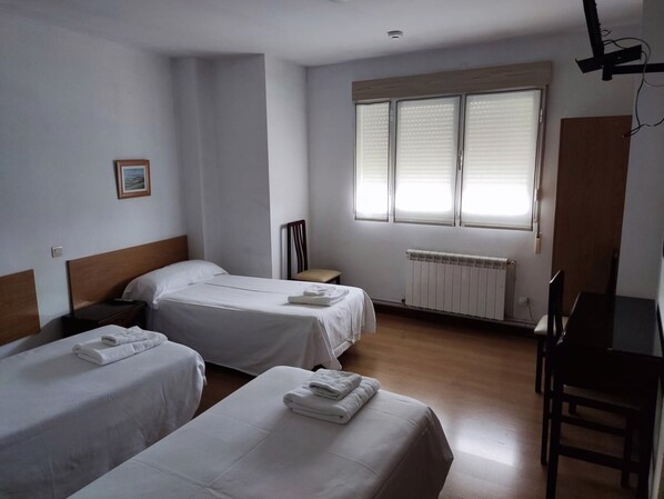 A hotel room with two single beds, a wooden headboard, a small bedside table, a chair, a radiator, and a window with blinds. - Pensión Las Matillas (Miranda de Ebro)