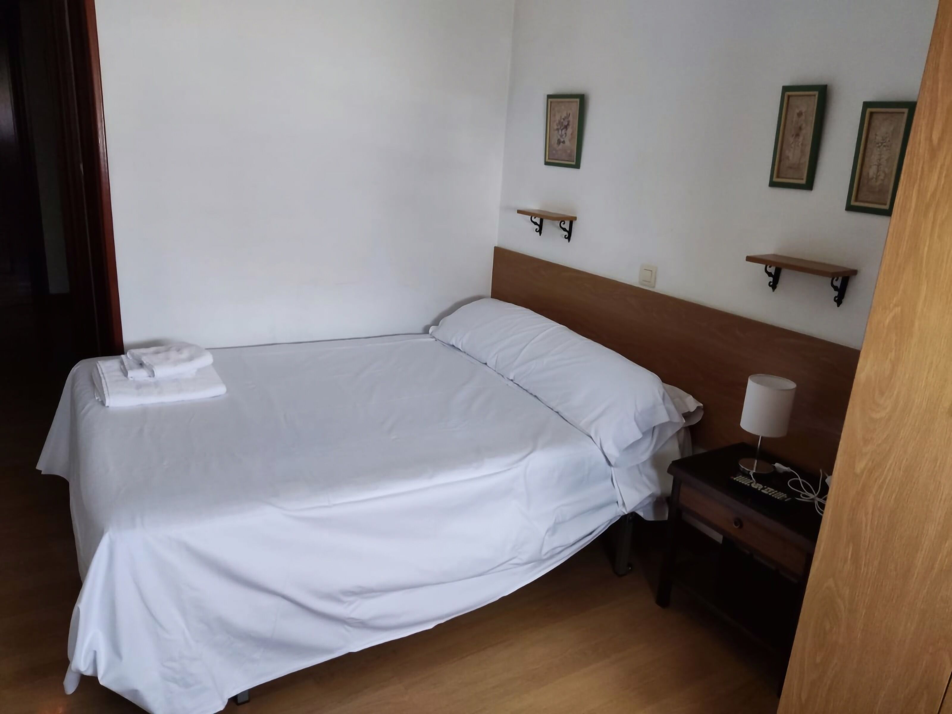 Ein ordentlich bezogenes Bett mit weißen Leinen, ein hölzernes Kopfende und ein Nachttisch mit Lampe.