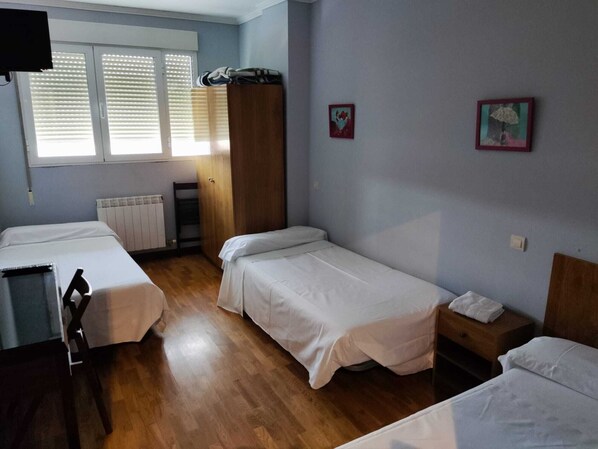 A room with two single beds, a wooden wardrobe, a radiator, and a window with blinds. - Pensión Las Matillas (Miranda de Ebro)