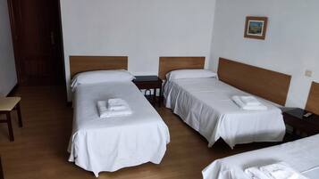 Een hotelkamer met drie enkele bedden, houten hoofdborden, wit beddengoed en een kleine tafel met een afstandsbediening.