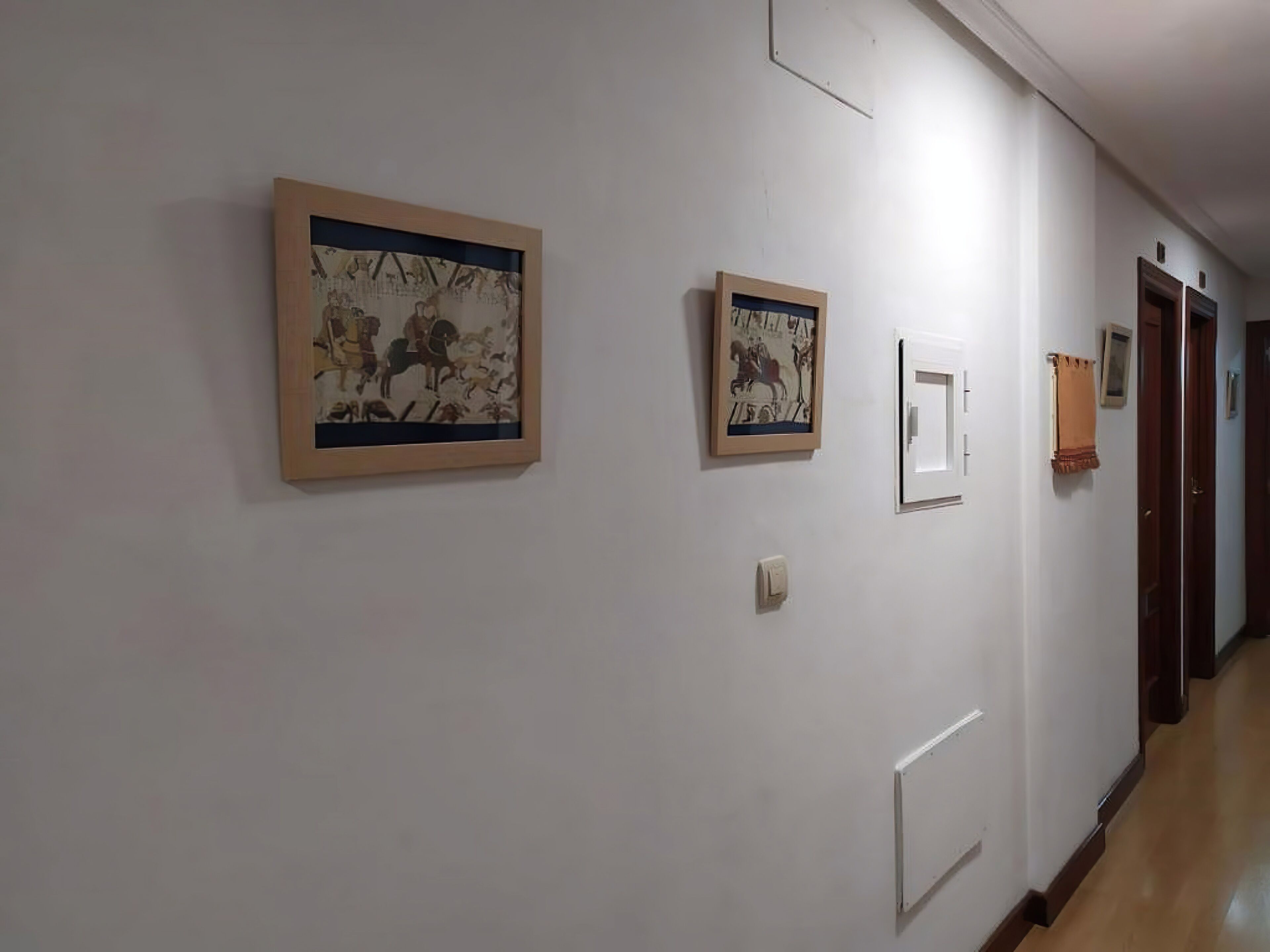 Un couloir avec des œuvres d’art accrochées aux murs, un interrupteur et une porte au bout.