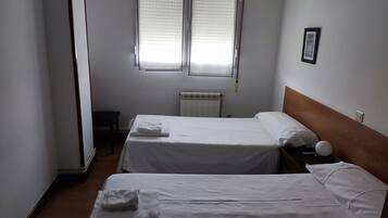 Une chambre d’hôtel avec deux lits, un radiateur, une fenêtre avec des stores et un tableau encadré au mur.