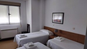 A hotel room with two single beds, a wooden headboard, a framed picture on the wall, and a window with blinds. - Pensión Las Matillas (Miranda de Ebro)