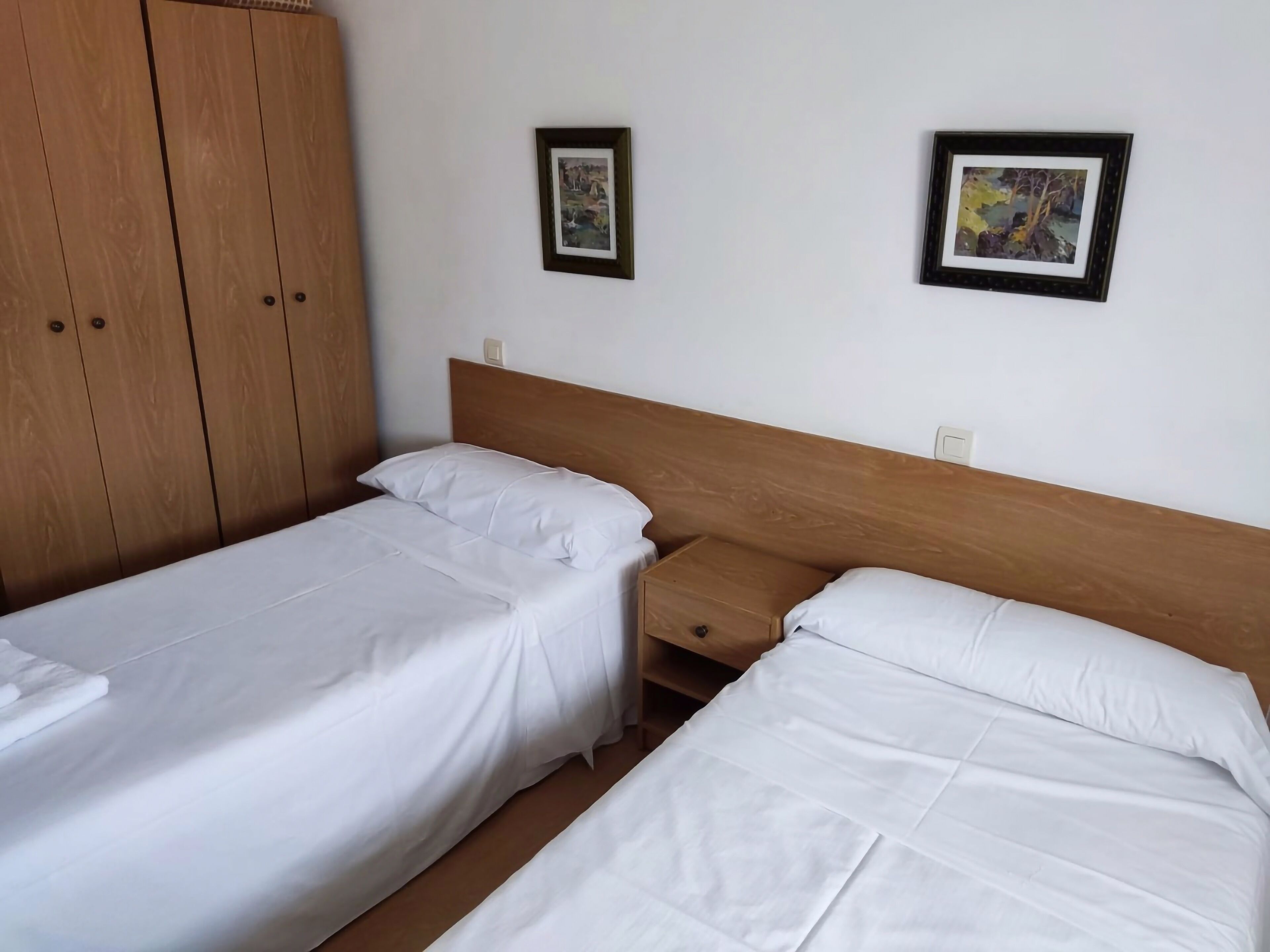 Habitación de hotel con dos camas individuales, un armario de madera y dos cuadros en la pared.