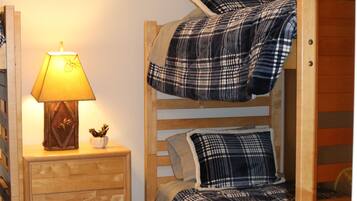 A bunk bed with plaid bedding, a bedside lamp, and a small plant on a wooden nightstand.