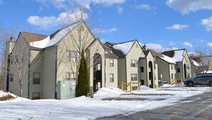 A row of multi-story residential buildings with a snow-covered ground, a parked car, and a clear sky.