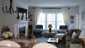 A living room with a fireplace, two armchairs, a sofa, and a dining table with chairs.
