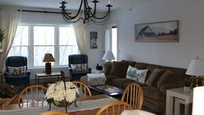 A living room with a brown sofa, two blue armchairs, a wooden coffee table, and a chandelier.