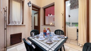 A dining area with a tiled table set for four, a kitchen visible through an open door, and a small outdoor seating area with a table and chairs. - I Tre Golfi Luna Turca Apartment (San Vito Lo Capo)