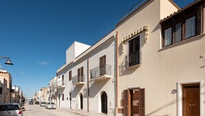 A street view of a residential area with buildings featuring balconies, wooden doors, and a clear blue sky. - I Tre Golfi Luna Turca Apartment (San Vito Lo Capo)