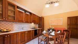 A kitchen with wooden cabinets, a tiled backsplash, a dining table with chairs, and a chandelier. - I Tre Golfi Luna Turca Apartment (San Vito Lo Capo)