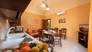 A compact kitchen with a sink, stove, and dining area with chairs and a table. - I Tre Golfi Luna Turca Apartment (San Vito Lo Capo)