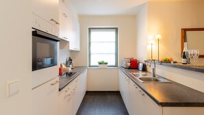 A modern kitchen with white cabinets, a built-in oven, a microwave, a sink, and a window with a plant.