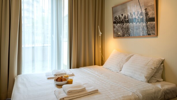 A hotel room with a neatly made bed, a breakfast tray with croissants and orange juice, and a framed historical photograph on the wall.