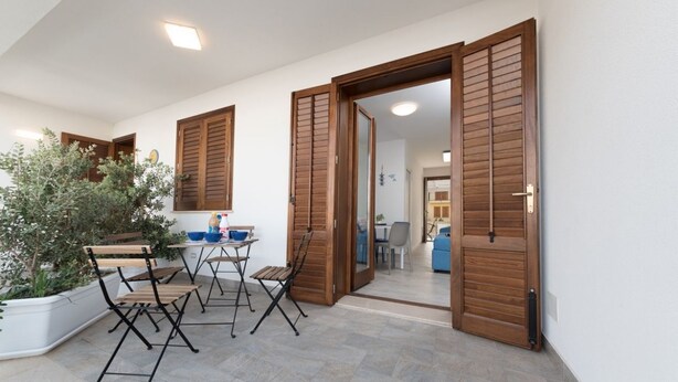Un espace de vie à aire ouverte comprenant une table et des chaises, des volets en bois et une plante en pot.