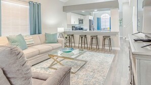 A modern living room with a sofa, coffee table, and a kitchen area in the background.