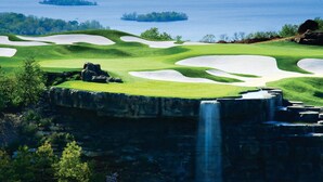 A golf course with sand bunkers, a waterfall, and a lake in the background.