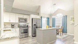 A modern kitchen with white cabinets, stainless steel appliances, and a marble countertop.