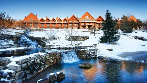 A lodge with a stone waterfall and snow-covered landscape.