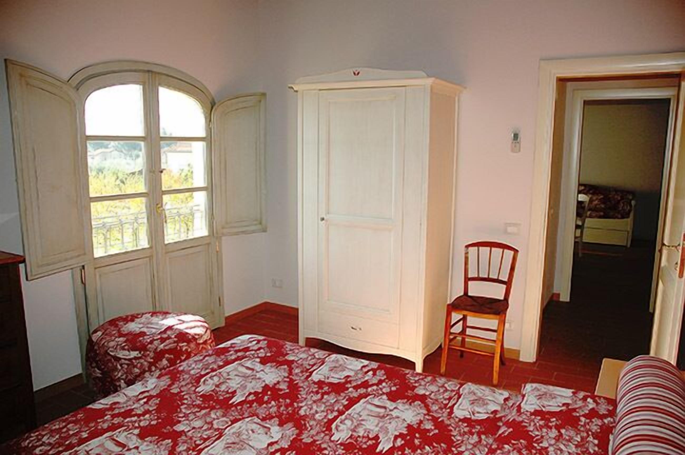 Un dormitorio con cama, armario, silla y puerta que da a otra habitación.