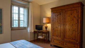 A bedroom with a bed, a wooden wardrobe, a desk with a computer, and a window with curtains.