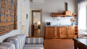 Ein gemütliches Wohnzimmer mit einer Couch und einem Esstisch, eine Küche mit Holzschränken und einer Mikrowelle, sowie ein Flur, der zu einem weiteren Raum führt.