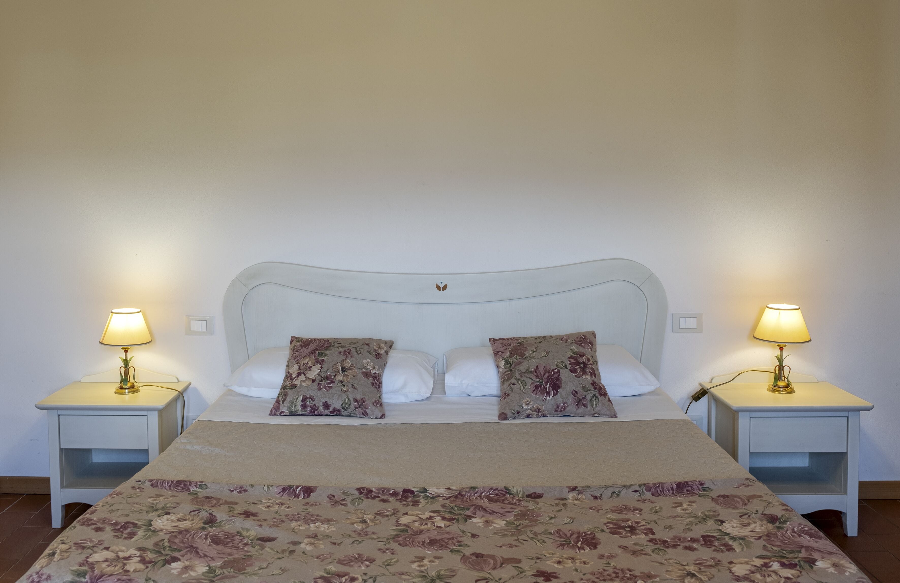 Ein Bett mit blumigem Überwurf, zwei Kissen und zwei Nachttischlampen.