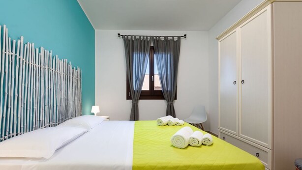 A hotel room with a bed, a wardrobe, a window with curtains, and a wall decoration.