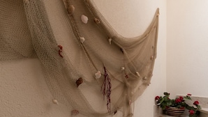 A beige woven fabric draped over a textured wall, with seashells and dried plants attached.