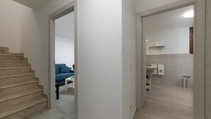 Eine Treppe führt zu einem Wohnbereich mit einem blauen Sofa und einem kleinen Tisch. Durch eine offene Tür ist eine Küche erkennbar.