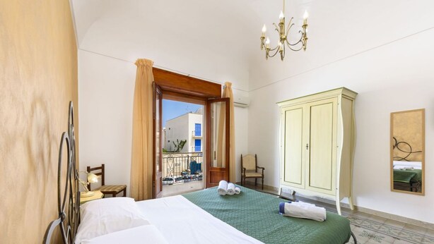 Ein Hotelzimmer mit Bett, Kleiderschrank, Stuhl, kleinem Tisch mit Lampe und Blick auf den Balkon.