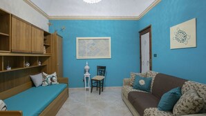A room with a blue wall, a wooden cabinet, a sofa, a patterned couch, a chair, and a small table with a decorative item.