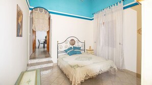 A bedroom with a bed, a nightstand, a chair, and a staircase leading to another room.