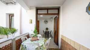A narrow corridor with a table and chairs, a potted plant, and a door leading to another room.