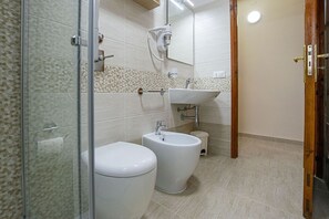 Une salle de bain équipée de toilettes, d’un bidet et d’une douche à parois de verre.