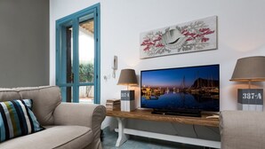 A living room with a beige sofa, a wooden coffee table, a flat-screen TV, and a painting above it. - I Tre Golfi Villa Iride (San Vito Lo Capo)