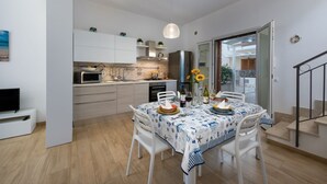 Uma cozinha moderna com armários brancos, uma mesa de jantar posta com pratos e copos, e uma luminária pendente.
