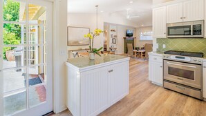Une cuisine moderne avec des meubles blancs, un îlot central et un coin repas doté de chaises en osier.