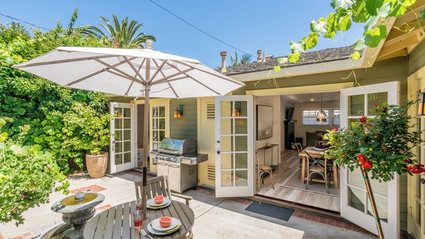 Une terrasse extérieure avec une table à manger, des chaises, un barbecue et une plante en pot.