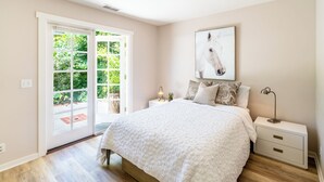 Une chambre avec un grand lit, une table de chevet, une lampe et une fenêtre donnant sur un paysage verdoyant.