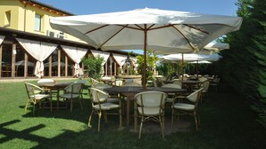 An outdoor patio with tables and chairs, covered by large umbrellas, and surrounded by greenery. - Osteria e Locanda del Viaggiatore (Russi)