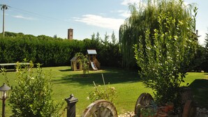 A grassy area with a small wooden playhouse and a slide, surrounded by trees and greenery. - Osteria e Locanda del Viaggiatore (Russi)