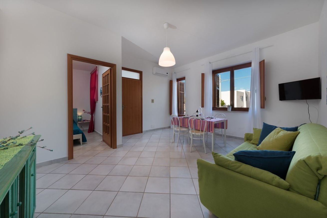 Un vaste espace de vie comprenant un canapé vert, une table à manger avec des chaises et un téléviseur fixé au mur.