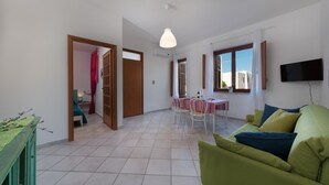 Un vaste espace de vie comprenant un canapé vert, une table à manger avec des chaises et un téléviseur fixé au mur.