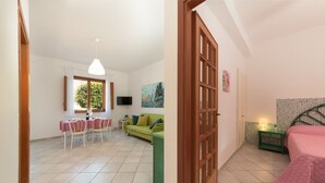 Une pièce comprenant un coin repas, un canapé vert, un lit avec une couvre-lit rose et un téléviseur fixé au mur.