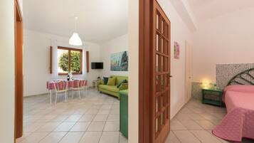 Una habitación con comedor, un sofá verde, una cama con edredón rosa y un televisor en la pared.