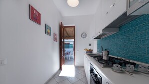Une cuisine moderne avec des meubles blancs, un pare-feu turquoise et une cuisinière à gaz. On peut voir des tableaux encadrés au mur et une horloge.