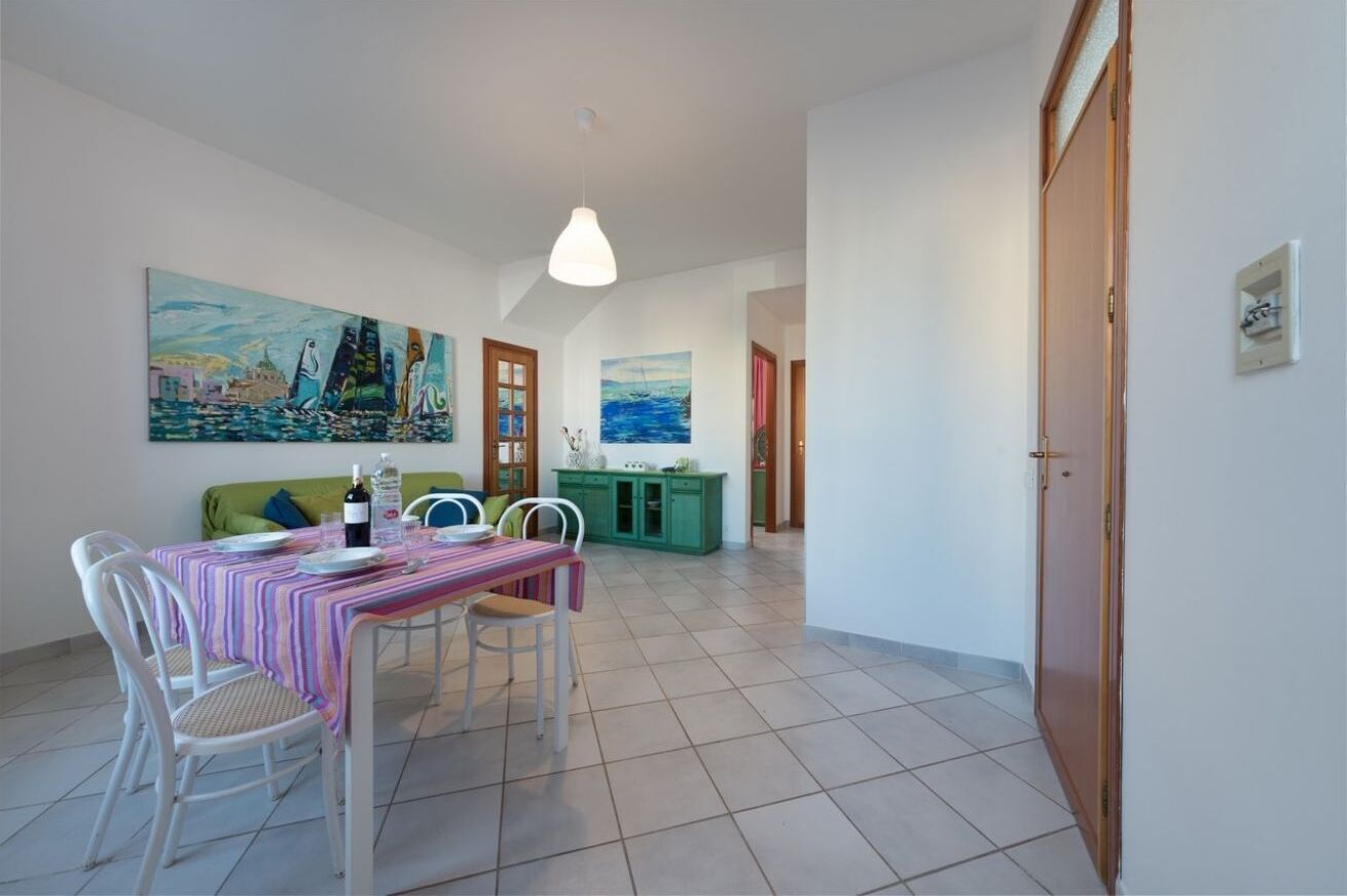 Un coin repas avec une table dressée pour deux personnes, des chaises, un canapé vert et deux tableaux accrochés au mur.