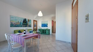 Un coin repas avec une table dressée pour deux personnes, des chaises, un canapé vert et deux tableaux accrochés au mur.